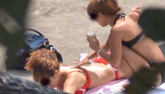 砂浜で日光浴、オイルの塗りっこする女子二人