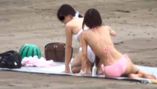水着ギャル二人が砂浜にシートを敷いて日光浴